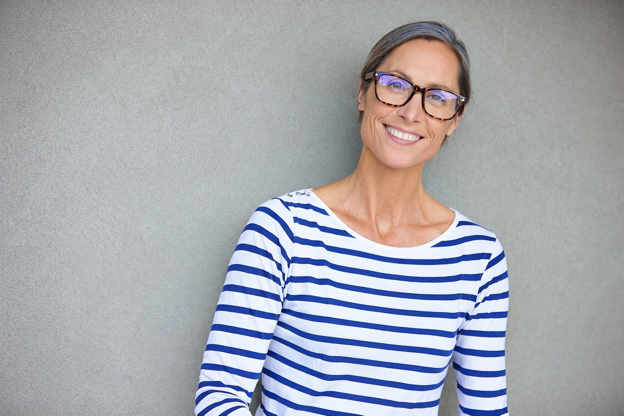Mujer con anteojos y camiseta a rayas junto a una pared gris