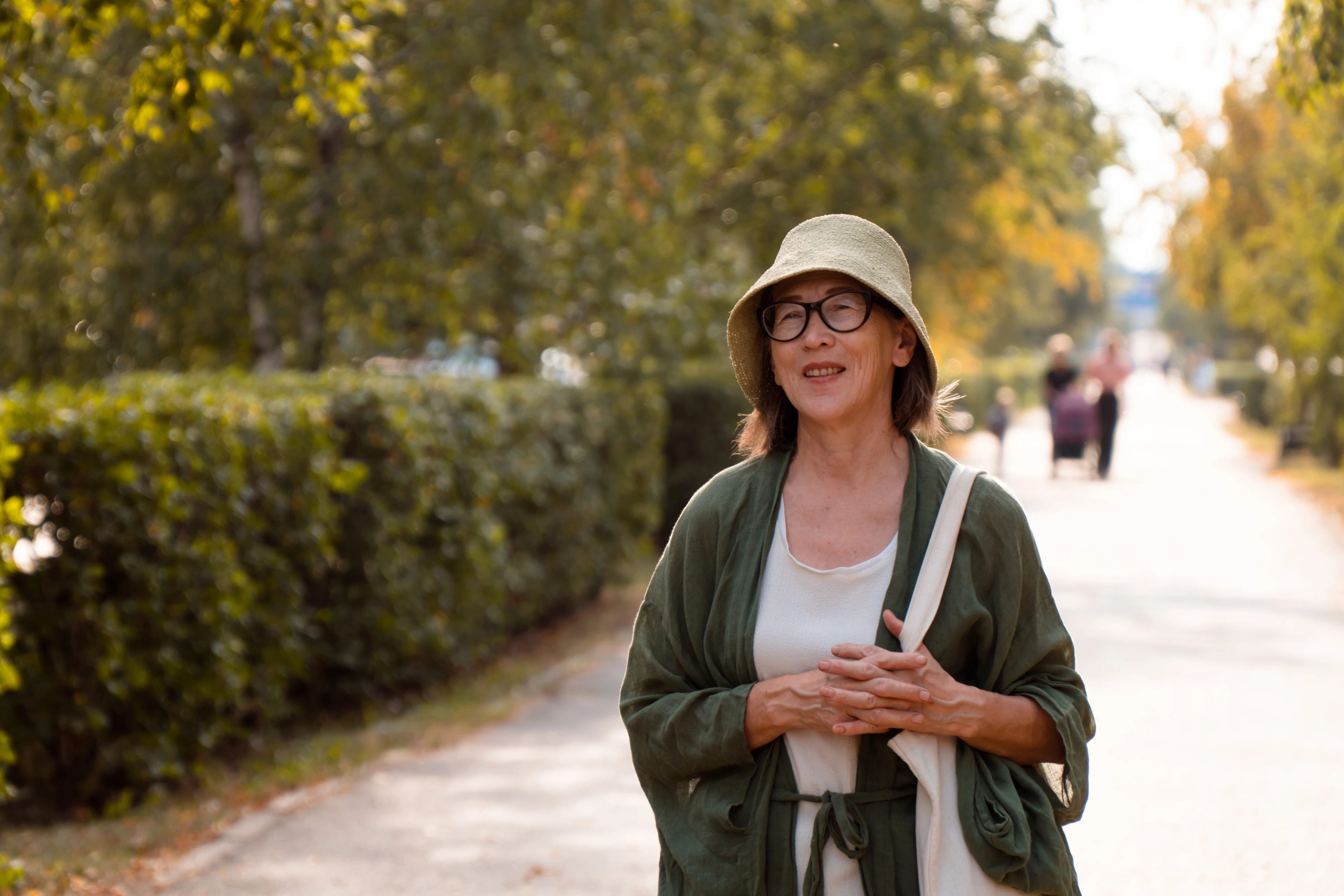 Mujer con anteojos y sombrero caminando por un parque